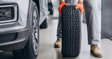 Mecanic ținând o anvelopă lângă mașină, într-un service auto.