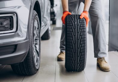 Mecanic ținând o anvelopă lângă mașină, într-un service auto.