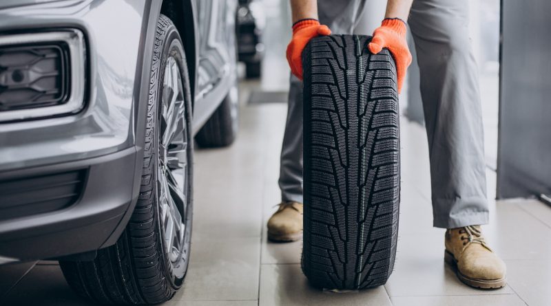 Mecanic ținând o anvelopă lângă mașină, într-un service auto.