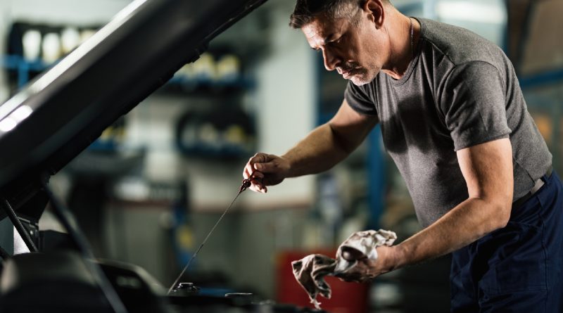 Mecanic verificând nivelul uleiului de motor cu joja, într-un service auto